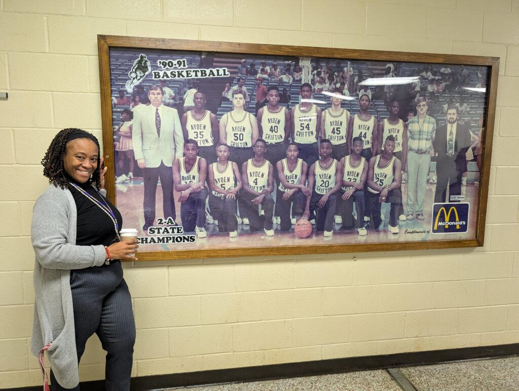 Jacqui Allen, Southeast Lead for the GRAD Partnership ECU cohort schools stands next to a picture of herself as a cheerleader for the 1990-1991 state basketball championship team from Ayden-Grifton High School.